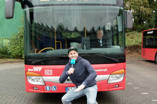Ein Mann mit Mikrofon posiert vor einem roten Bus