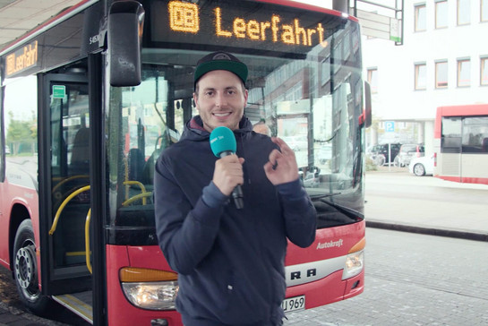 Ein Mann steht mit seinem Mikro vor einem Bus