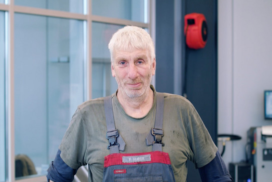 Ein älterer KFZ Mechaniker lacht in die Kamera