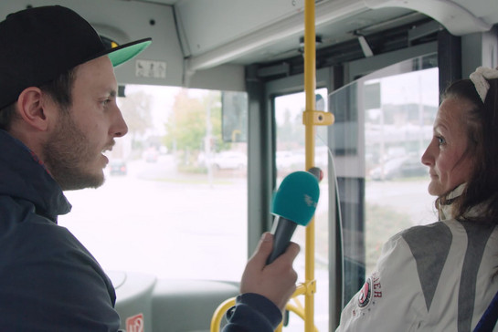 Ein Mann interviewt eine Frau die vorne im Bus sitzt