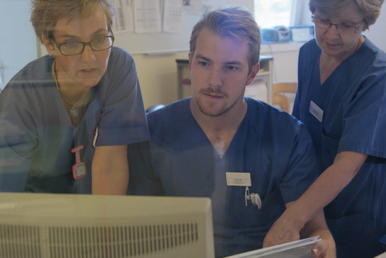 Drei Krankenpfleger stehen vor einem Computer