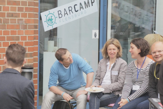Eine Personengruppe sitzt vor dem Barcamp Flensburg und unterhält sich