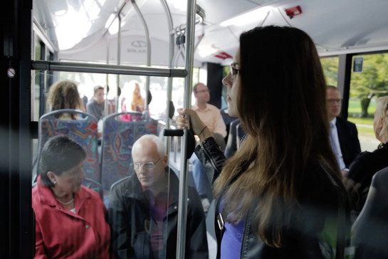 In einem Stadtbus mit vielen Fahrgästen, eine Passagierin steht an der Tür. 