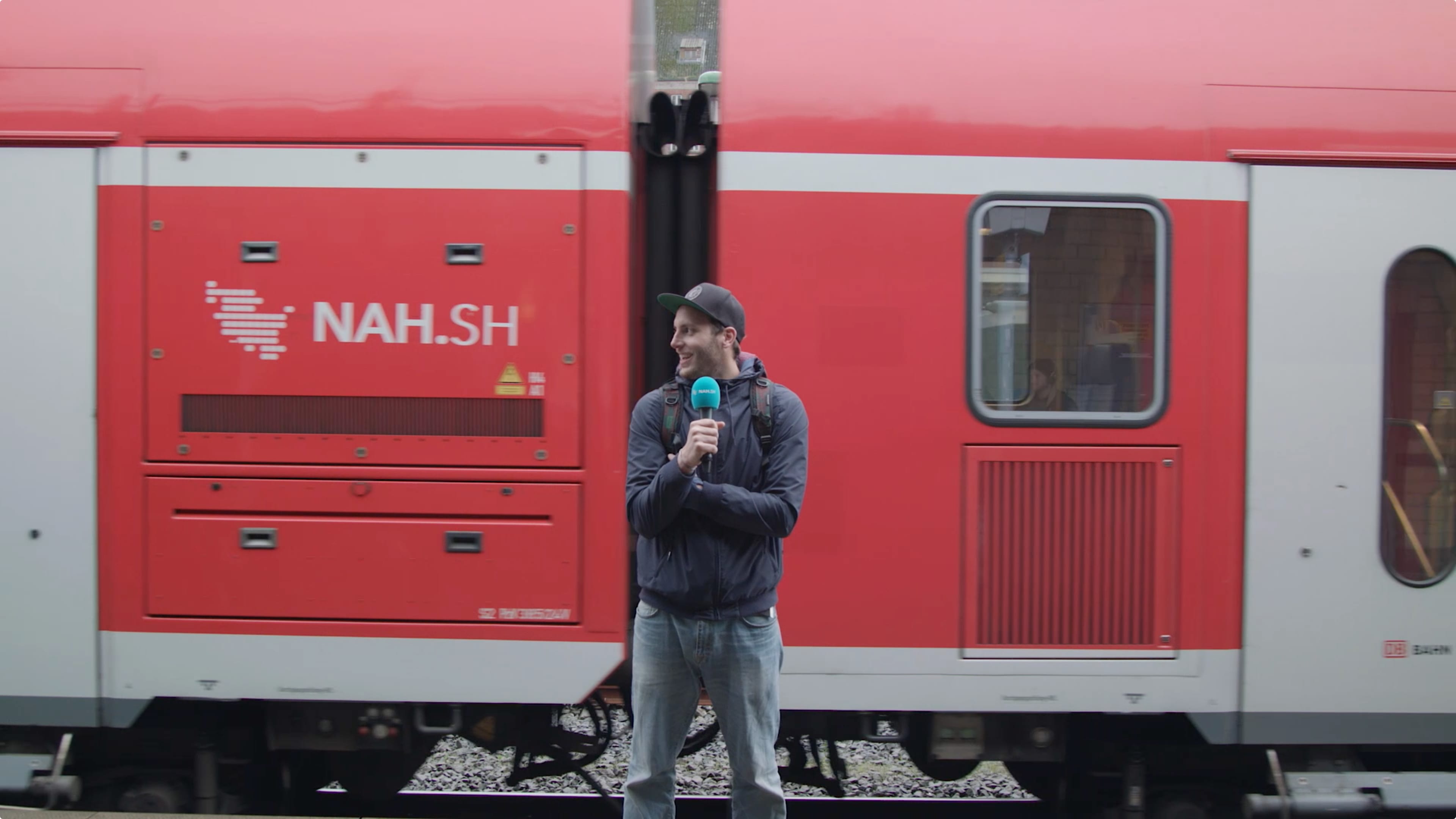 Ein Mann mit Mikrofon steht vor einem roten Zug