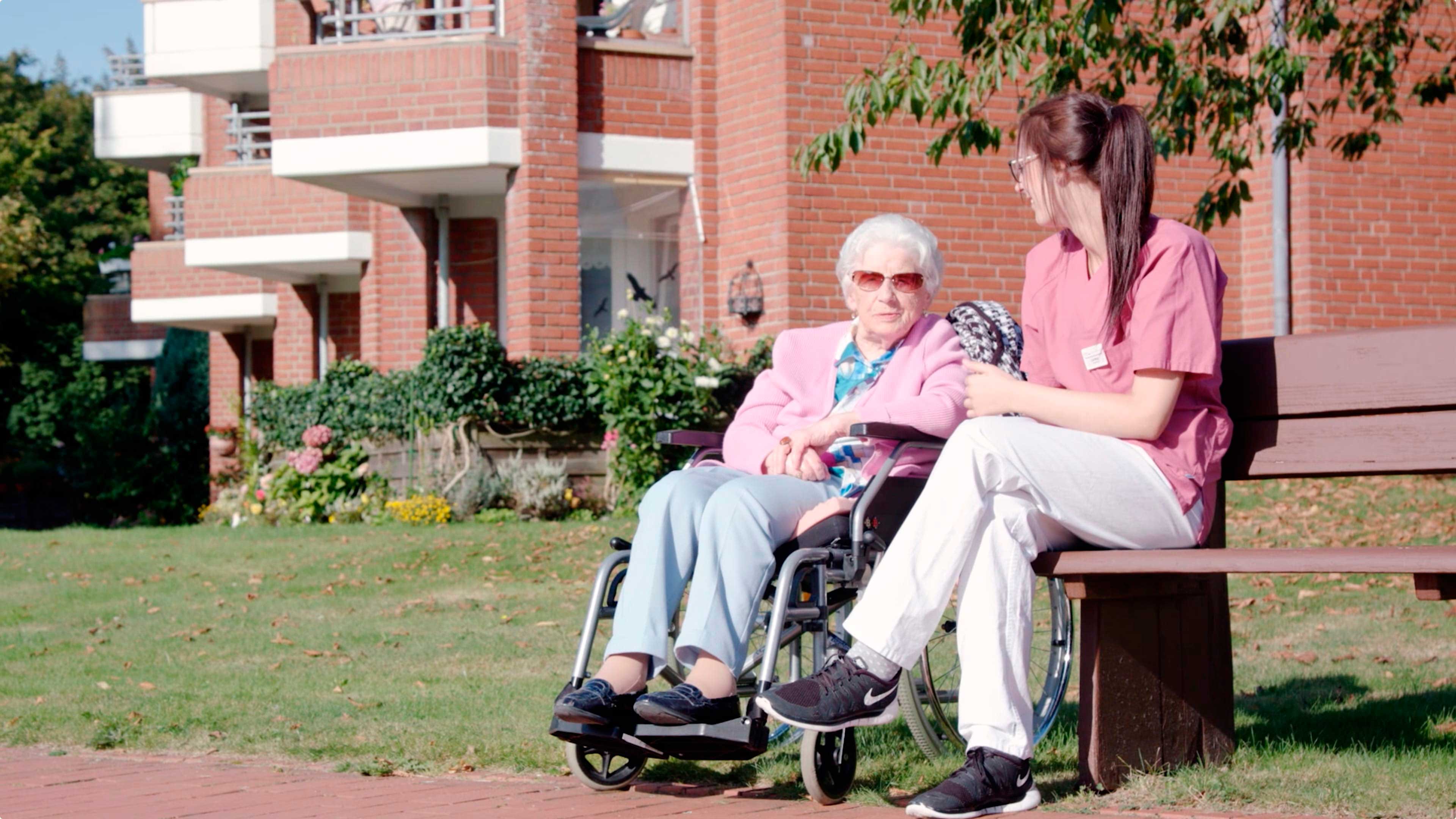 Eine Altenpflegerin sitzt mit einer älteren Dame im Garten