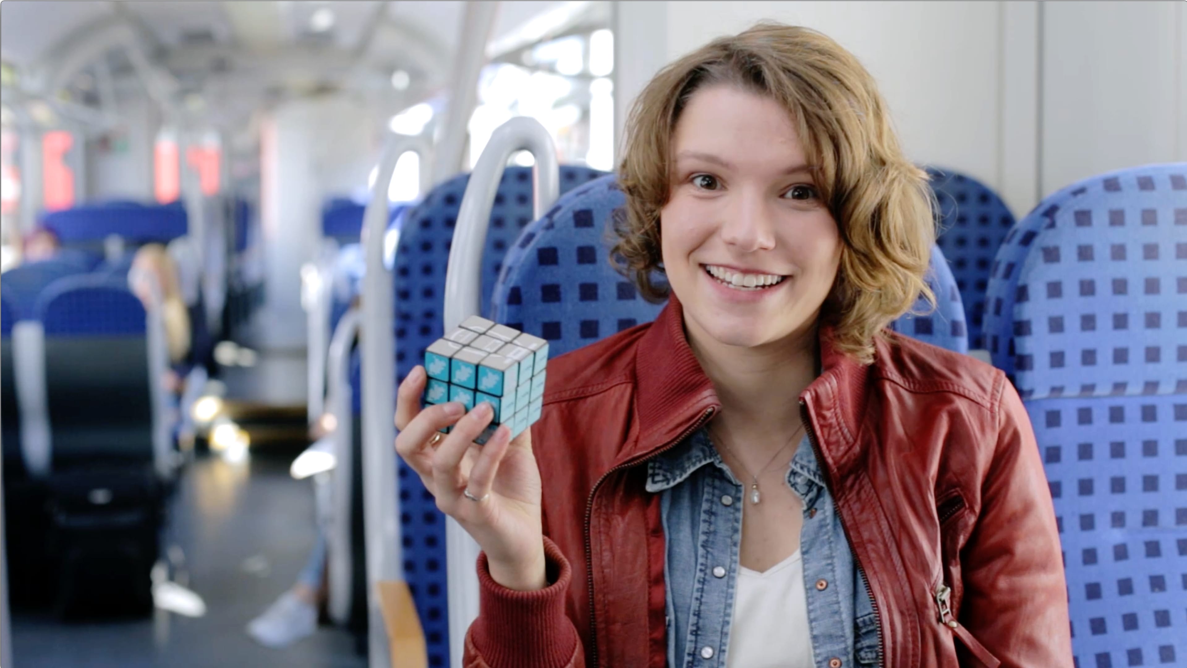 Eine Frau sitzt in Zug und hält einen Cube hoch