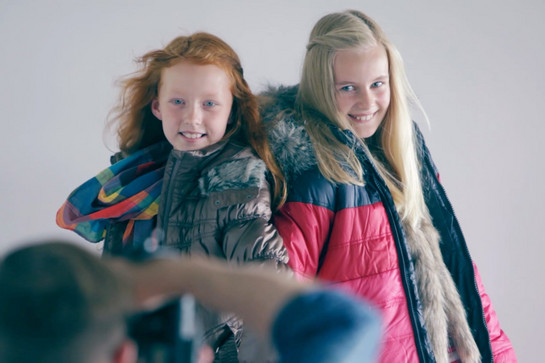 bb_modelbehrens_teaser_05_hauptteaser.jpg Ein Fotograf fotografiert zwei junge Mädchen, die Winterkleidung tragen.