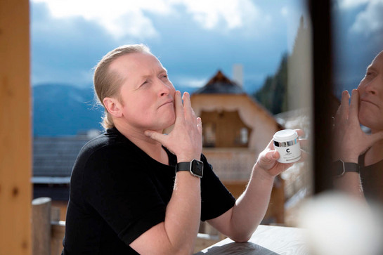 bb_cellagon_teaser_01.jpg Joey Kelly sitzt an einem Holztisch, in der Hand ein Körperpflegeprodukt. Er trägt ein schwarzes T-Shirt und eine Armbanduhr. Im Hintergrund blauer Himmel.