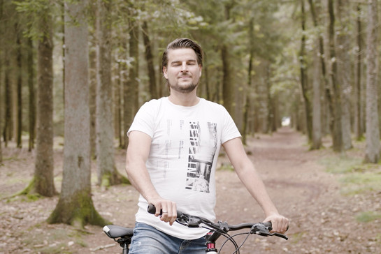 Mann mit Fahrrad im Wald atmet durch