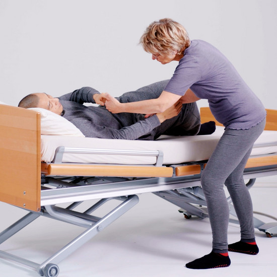 Eine Frau hilft einem Patienten aus dem Bett