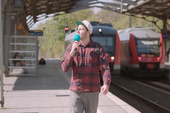 bb_bahnhofmission_teaser_02.jpg Ein Mann geht mit einem Mikro am Bahnsteig lang