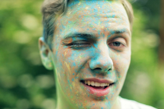 Ein junger Mann mit Farbe im Gesicht zwinkert in die Kamera