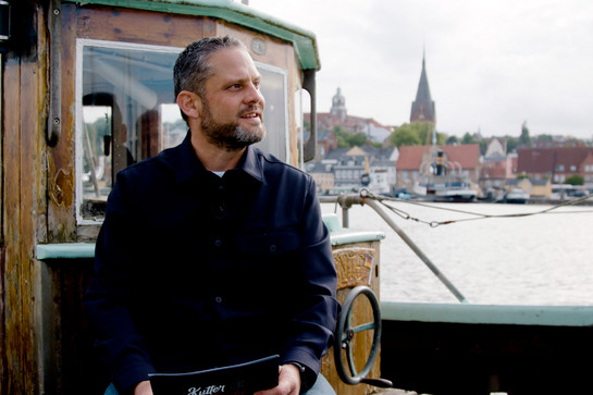 bb_buchholz_teaser_05.jpg Timo Klass sitzt auf einem hölzernem Schiff