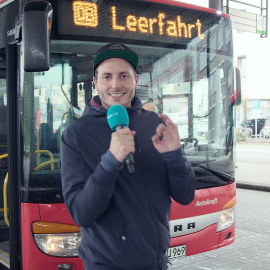 Ein Mann steht mit seinem Mikro vor einem Bus