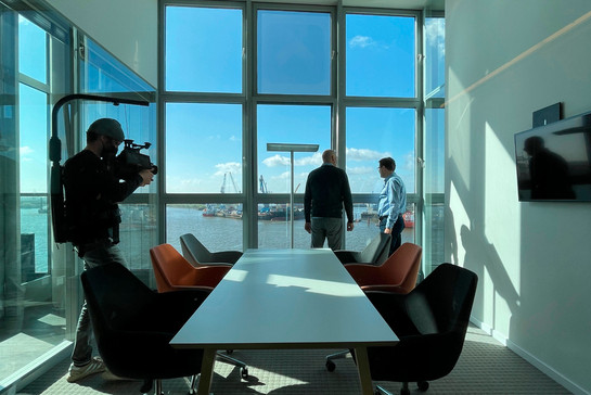 Kameramann filmt zwei Geschäftsmänner in einem Büro mit großem Fenster