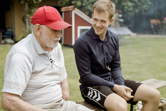 Ein alter Mann mit einer roten Cappy unterhält sich mit einem jungen Mann