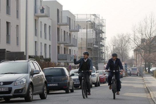 bb_sbv-vorstand_teaser_03.jpg Zwei Fahrradfahrer fahren an Wohnstraße vorbei an parkenden Autos