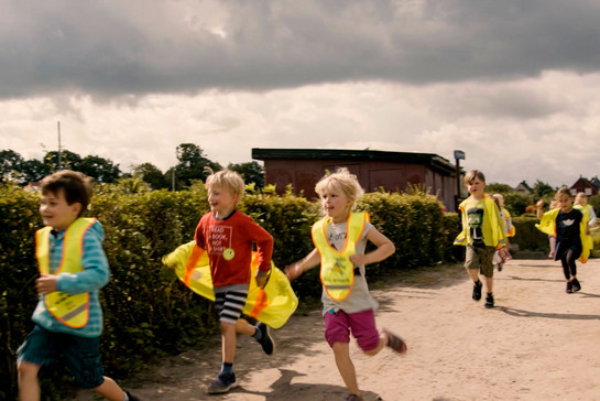 Mehrere Kinder laufen mit einer gelben schutzweste