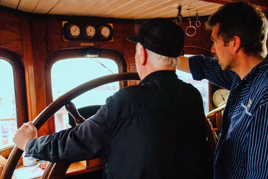 Zwei Männer stehen an einem Steuerrad eines Schiffes