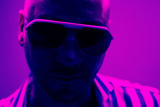 Ein Mann mit Sonnenbrille steht im lilanen Neonlicht