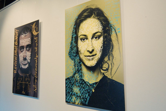 An der Wand hängen zwei große Portraits von einer jungen Frau und einem jungen Mann. Die Gesichter sind Worten und Symbolen zur Thematik der Ausstellung versehen. 
