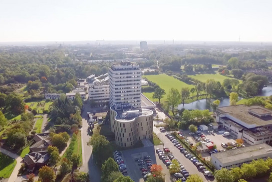 Luftaufnahme eines großen Gebäudes, davor ein Parkplatz. Es könnte die Universität in Kiel sein. 