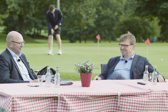Zwei Männer sitzen an einem Tisch der auf einem Golfplatz sitzt