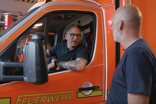 bb_feki_teaser_08.jpg Ein Feuerwehrmann lehnt sich aus dem Fenster des Feuerwehrautos