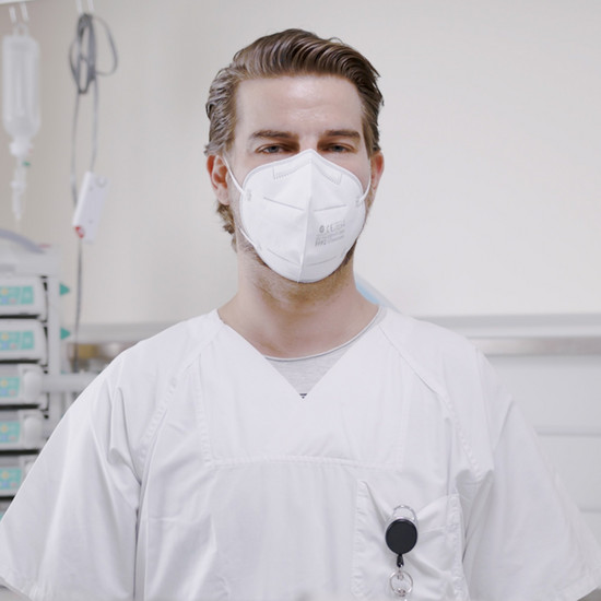 Männliche Pflegefachkraft in weißer Kleidung und weißer FFP2-Maske