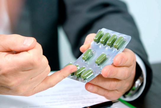 Ein Mann zeigt auf eine Tablettenpackung mit grünen Tabletten