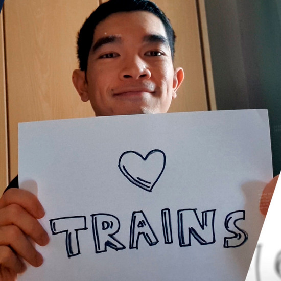 Ein Mann hält ein Schild in der Hand, darauf steht auf Englisch „Ich liebe Züge“.