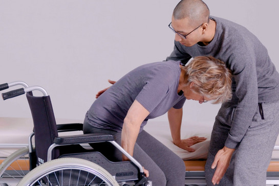 Ein Pfleger hilft einer Patientin aus dem Rollstuhl