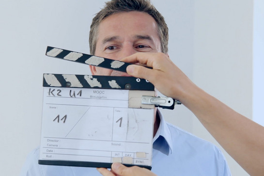 bb_mooc_teaser_01.jpg Eine Person hält eine Filmklappe vor einem Mann