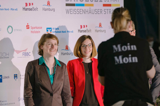 bb_fehmarnbelt_teaser_03.jpg Zwei junge Menschen vor einer Leinwand mit Sponsorenlogos
