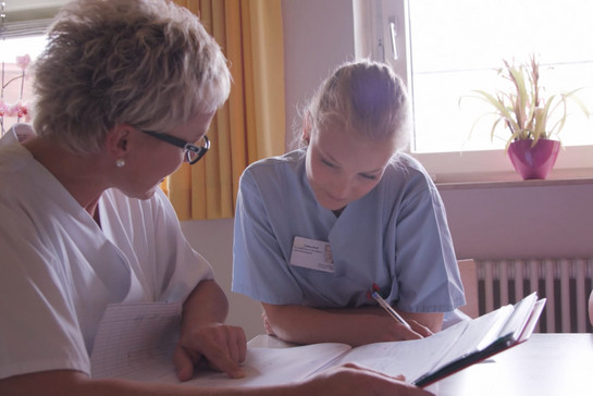 Eine Auszubildene und eine Krankenschwester sprechen miteinander