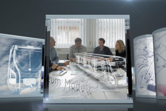 Fünf Personen an einem Schreibtisch, darauf ein computeranimiertes Bahnmodell. 
