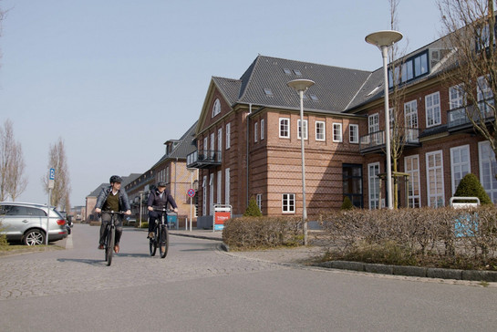 Zwei Fahrradfahrer mit Helm vor Häuserfront
