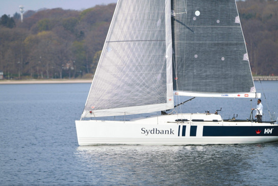 Zu sehen ist das Segelboot der Sydbank auf dem Wasser und mit Testimonial Sven Christensen an Bord.