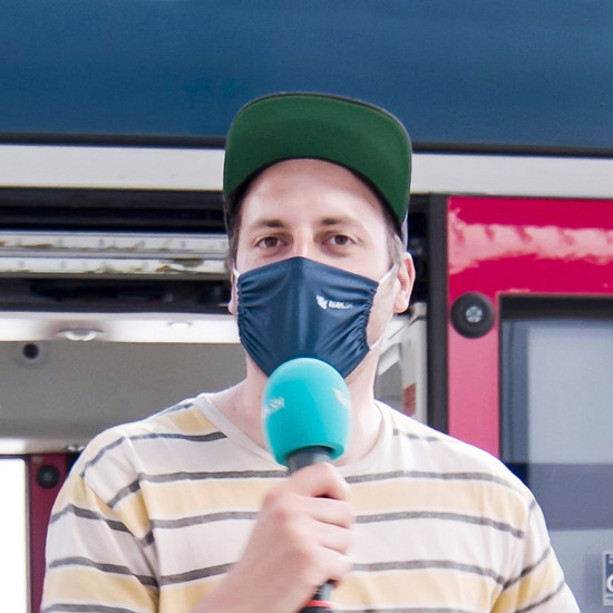 Ein Mann mit Maske spricht in sein blaues Mikrofon
