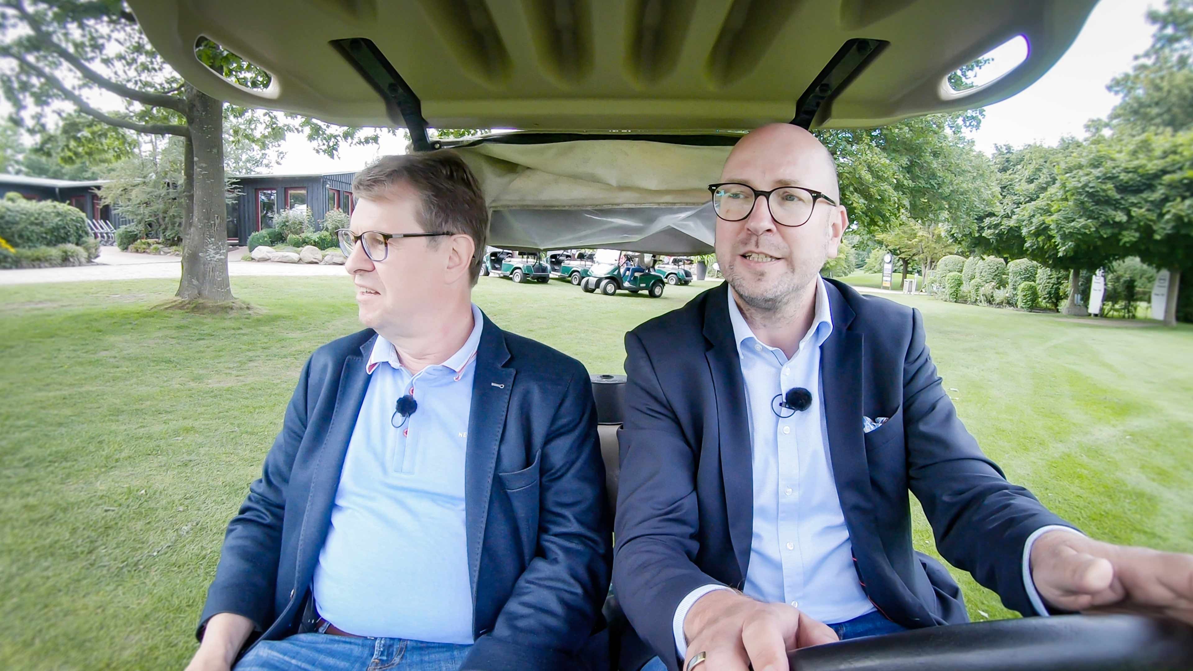 Zwei Männer im Anzug sitzen in einem Golfauto