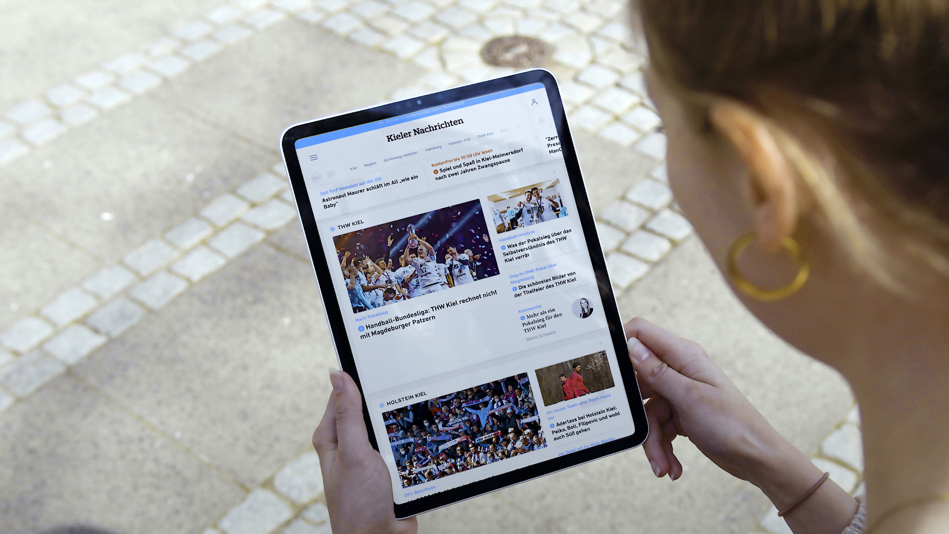 Blick über die Schulter einer Frau, die ein Tablet in der Hand hält, das die Website der Kieler Nachrichten zeigt